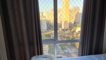 Quarto de hotel com cama, cortinas e vista para a cidade.