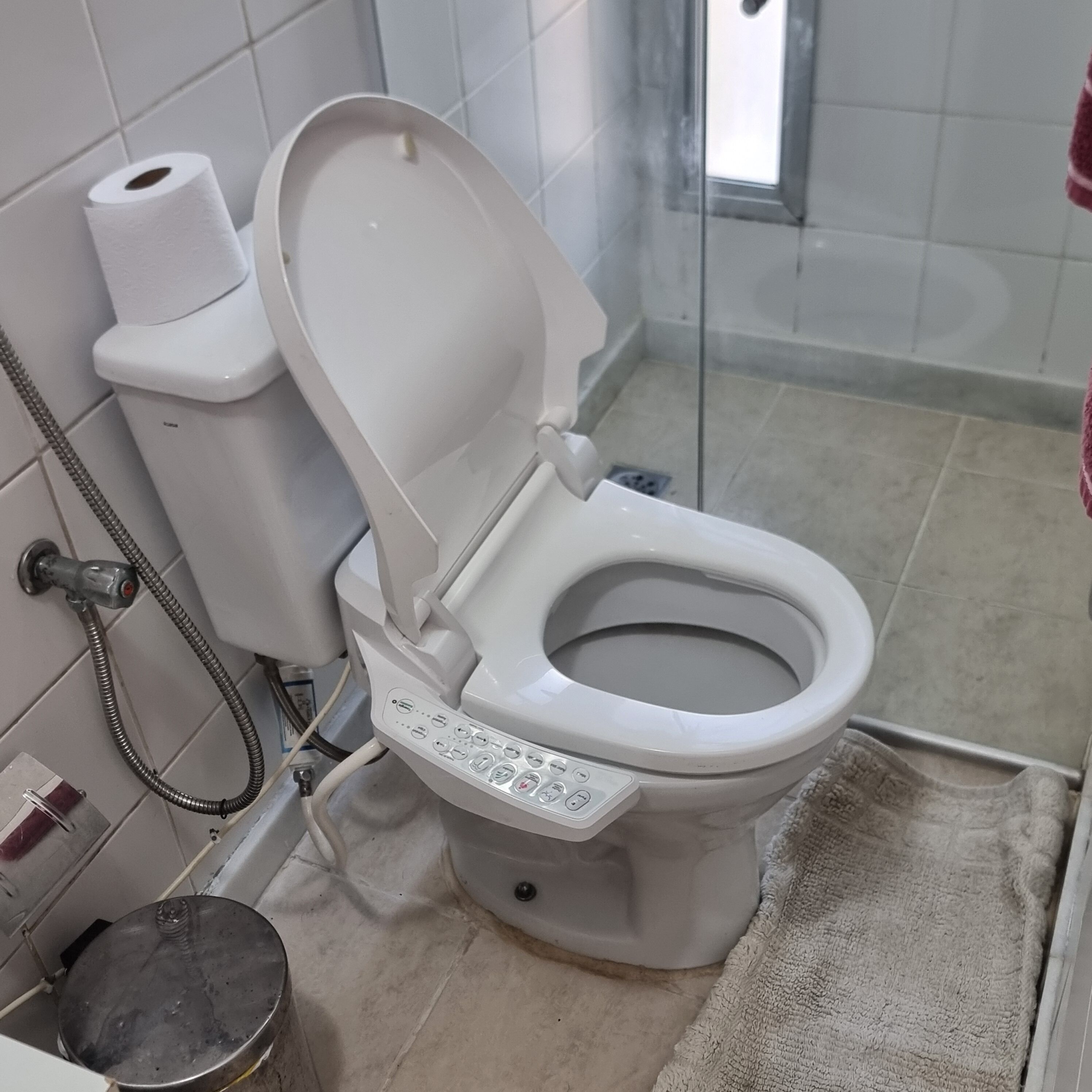 Casa de banho moderna com painel de controlo, suporte para papel higiénico e mangueira de chuveiro.