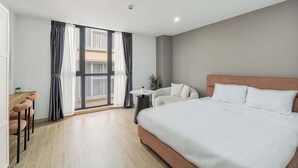 A hotel room with a large bed, a small table, a sofa, and a view of the outside through a large window.