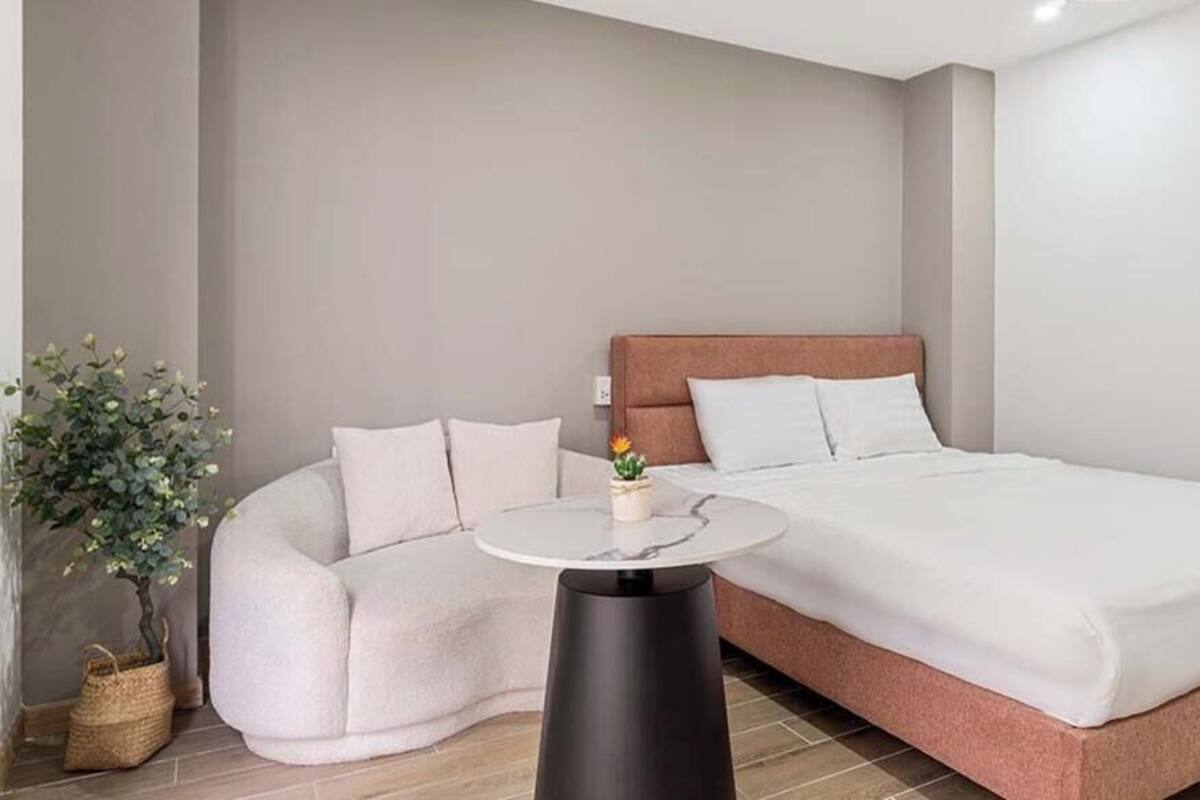 Un dormitorio con una cama, un rincón de descanso curvo, una pequeña mesa redonda y una planta en maceta.