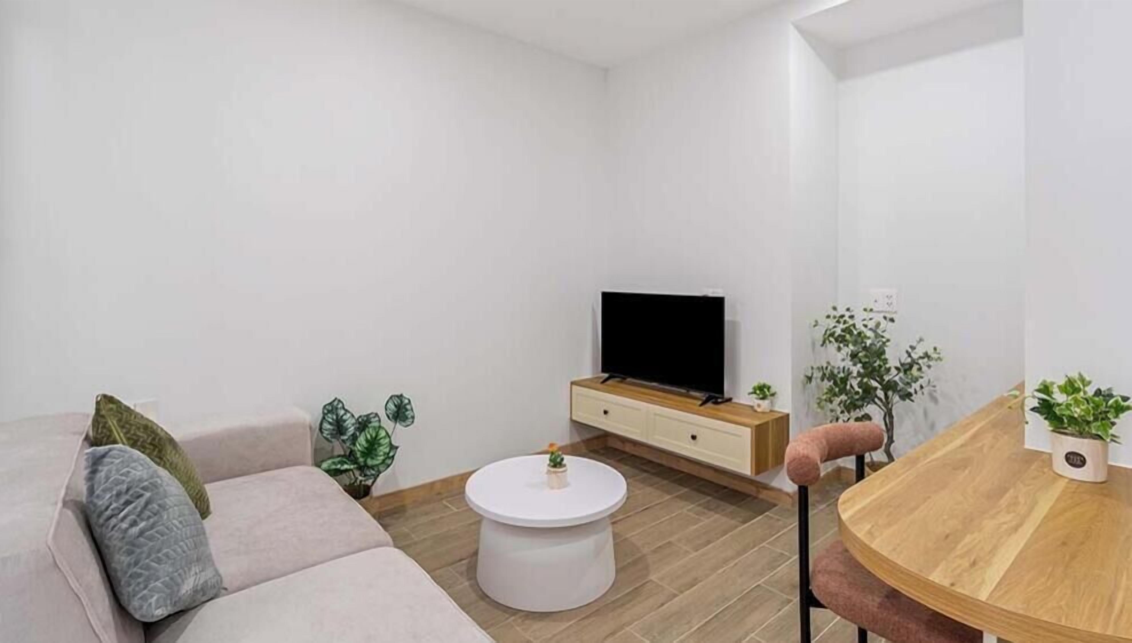 A modern living room with a sofa, a coffee table, a TV on a wooden cabinet, and a dining table with chairs.