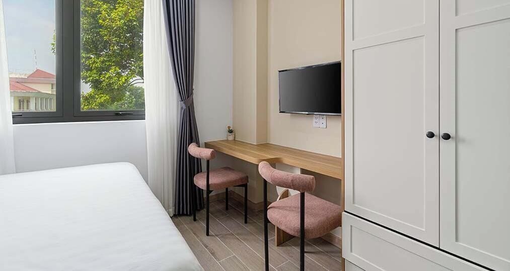 A hotel room with a bed, a desk with two chairs, a TV, and a wardrobe.