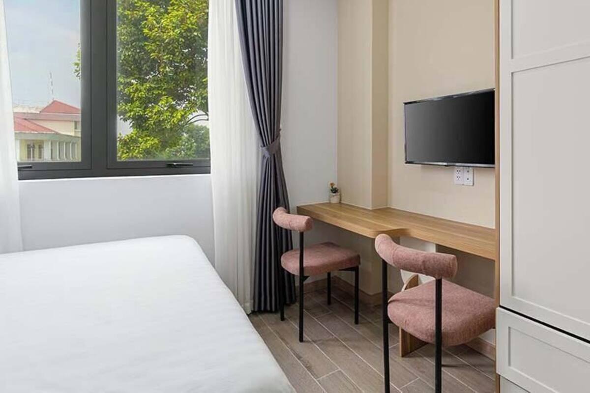 Un dormitorio con una cama, un escritorio con dos sillas, un televisor montado en la pared y un armario.