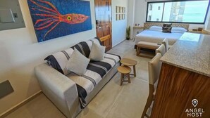 Ett modernt hotellrum med en soffa, ett litet bord, en säng och ett stort fönster.