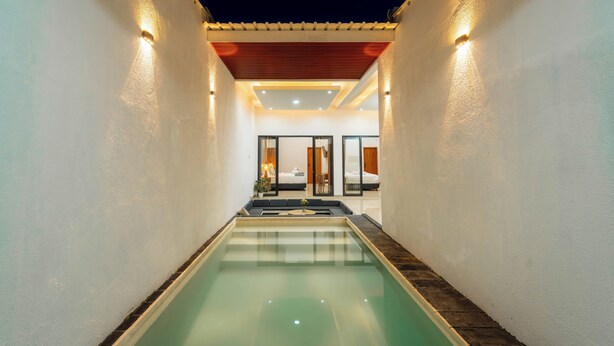 A swimming pool with a view of a bedroom and bathroom through glass doors. - Ghania Villas Melasti (Ungasan)