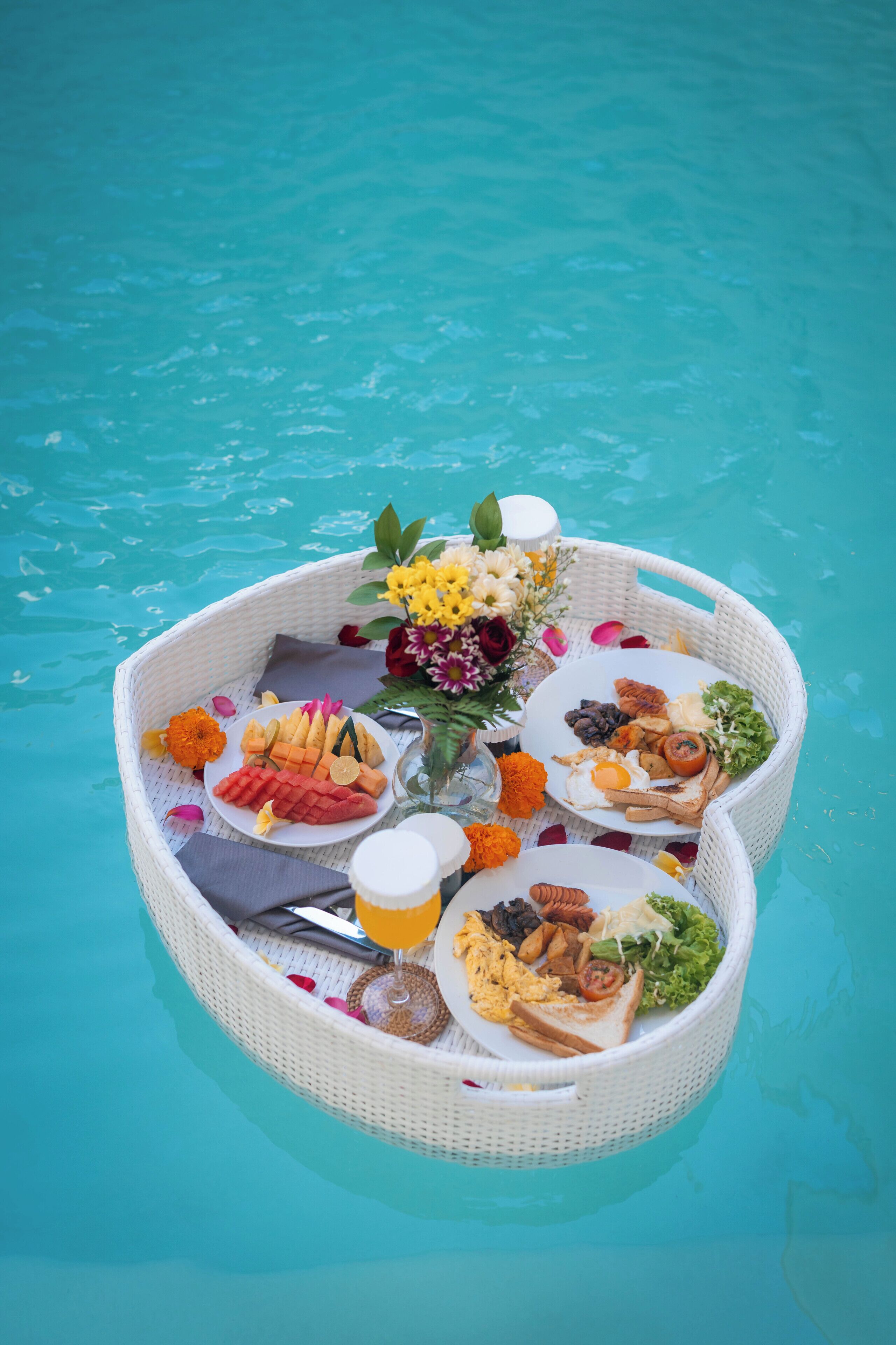 A floating dining setup with various food items and flowers on a pool.