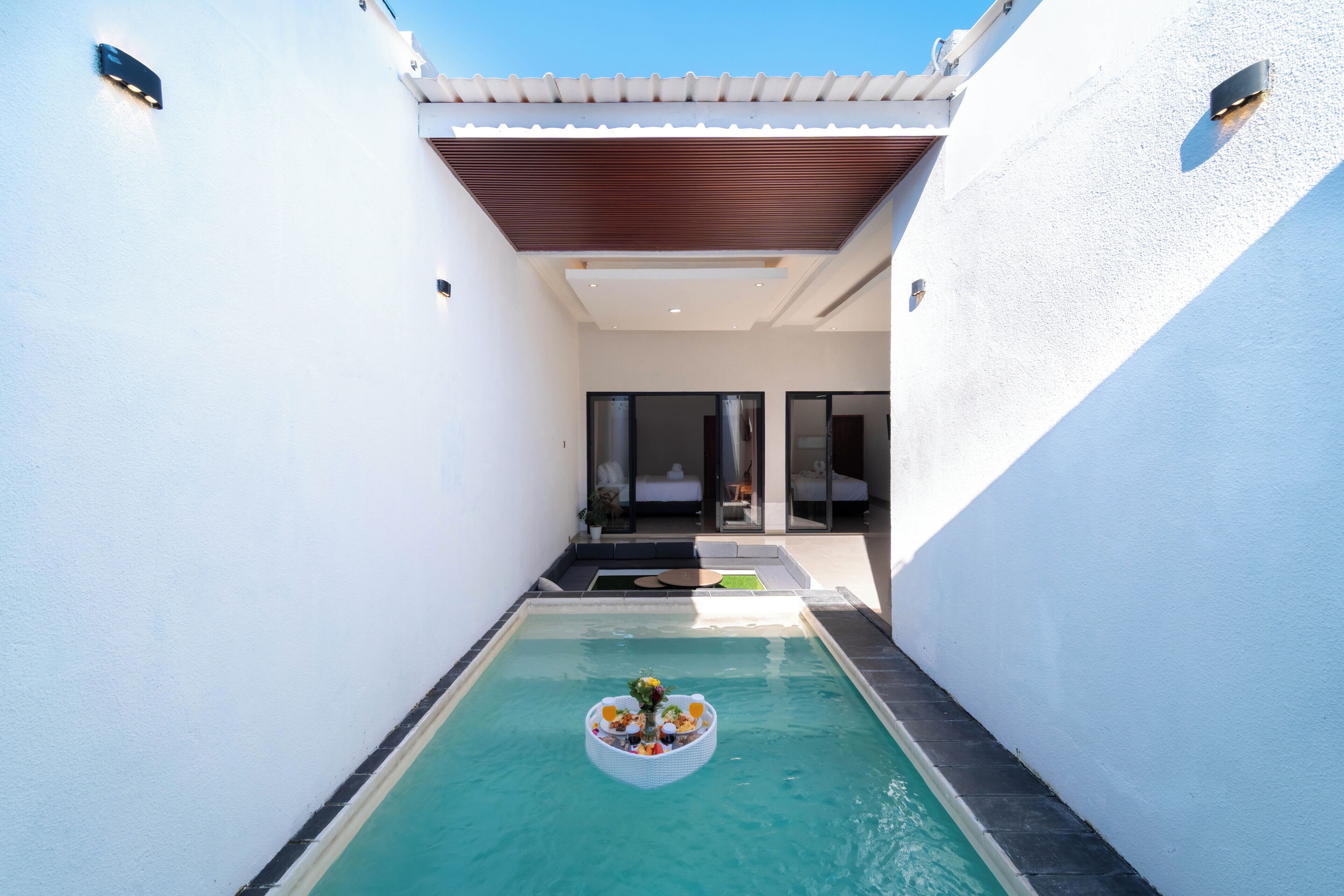 Un espace piscine moderne doté d’un bar flottant, d’un coin salon couvert et d’une vue sur l’intérieur.