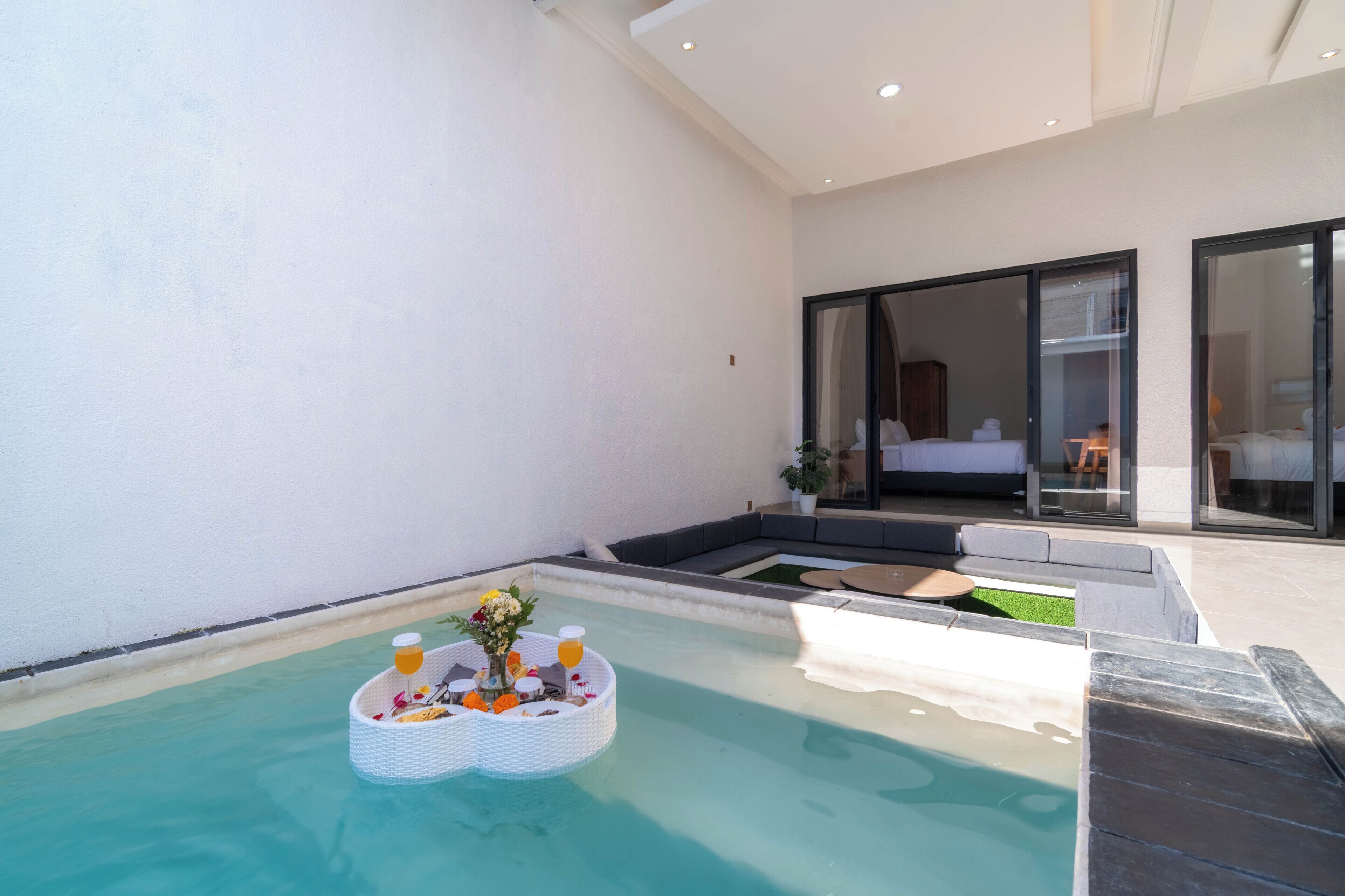 Ein modernes Hotelzimmer mit privatem Pool, Liege und einer großen Glasschiebetür zum Schlafbereich.