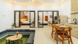 A modern hotel room with a sofa, dining table, and chairs, a small kitchen area, and a large mirror. - Ghania Villas Melasti (Ungasan)