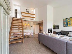 A spacious living area with a loft bedroom, a dining table, a sofa, and a television. - Nice beach house directly by the sea with garden (Nieuwvliet)