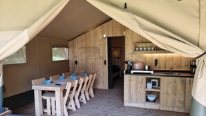 Un hébergement sous tente comprenant un espace repas, un coin cuisine et un espace nuit.