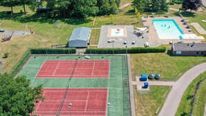 Vue aérienne d’un complexe sportif comprenant deux courts de tennis, une piscine et un espace couvert.