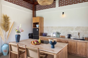Una cocina con una mesa de madera, sillas, un jarrón con flores y un frutero.