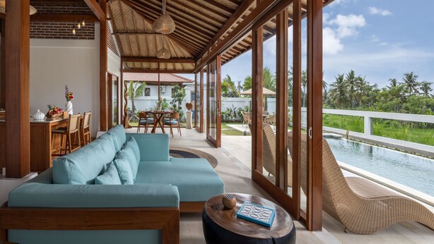 A spacious living area with a large sofa, a dining table, and a view of a pool. - Uma Dawa Residence (Ubud)