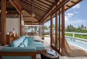 A spacious living area with a large sofa, a dining table, and a view of a pool. - Uma Dawa Residence (Ubud)