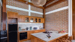 A kitchen with wooden cabinets, a black refrigerator, a marble island, and a sink. - Uma Dawa Residence (Ubud)