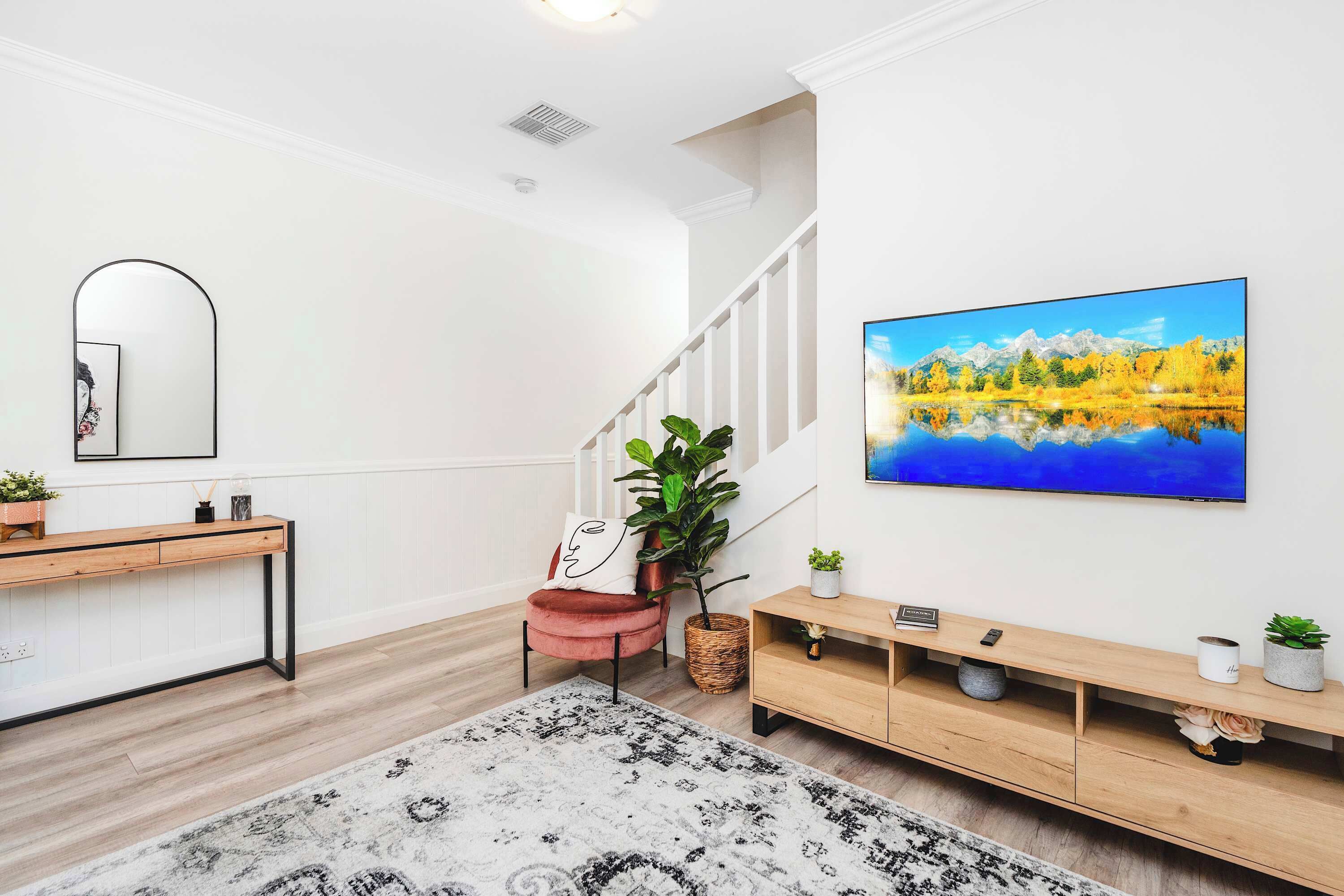 Un salon moderne avec un escalier, un grand tableau, une console en bois et une plante en pot.