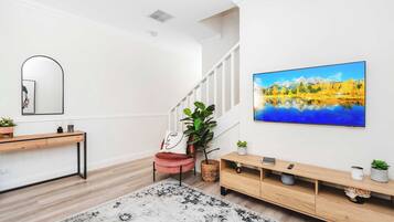 Un salon moderne avec un escalier, un grand tableau, une console en bois et une plante en pot.