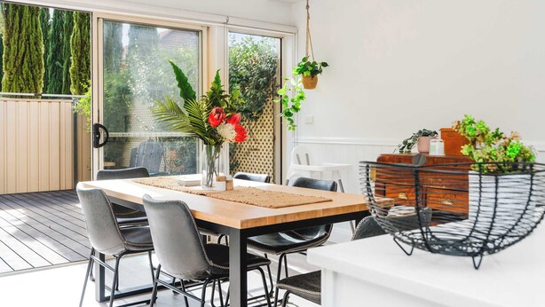 A dining area with a wooden table, grey chairs, a black metal chair, and a hanging plant. - Travers Townhouse - Close to CBD, Gated Community (Wagga Wagga)