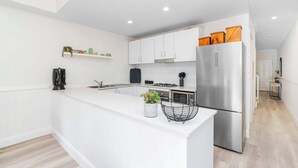A modern kitchen with white cabinetry, a stainless steel refrigerator, and a central island with a plant. - Travers Townhouse - Close to CBD, Gated Community (Wagga Wagga)