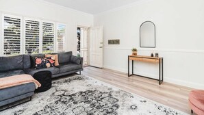 A modern living room with a grey sofa, a black ottoman, a patterned rug, a wooden console table, and a large mirror on the wall. - Travers Townhouse - Close to CBD, Gated Community (Wagga Wagga)