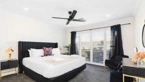 A modern hotel room with a large bed, a desk, a chair, a ceiling fan, and a view of the outside. - Travers Townhouse - Close to CBD, Gated Community (Wagga Wagga)