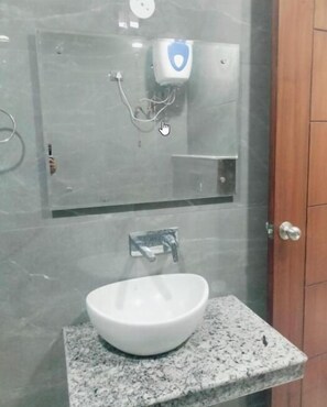 A bathroom with a white sink, a mirror, and a soap dispenser on the wall. - Hotel Golden Valley (Faridabad)