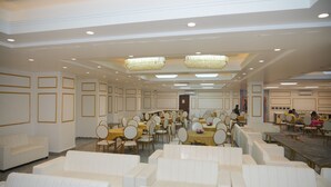 A spacious banquet hall with rows of white upholstered chairs and tables, chandeliers, and a central door. - Hotel Golden Valley (Faridabad)