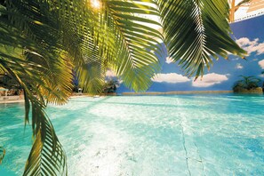 A clear blue pool surrounded by palm trees and a tropical beach scene.
