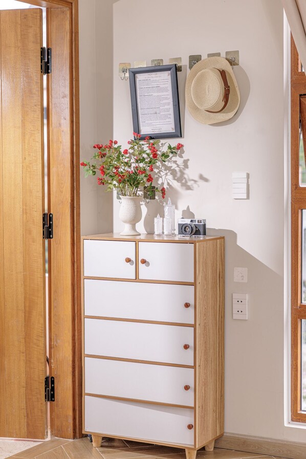 A wooden wardrobe with drawers, a vase with flowers, a camera, and a hat on the wall. - Lacle- BB's Garden (Xuan Huong - Da Lat)