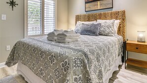 Une chambre à coucher comprenant un lit, une table de chevet, une lampe, une fenêtre avec des stores et une boussole fixée au mur.