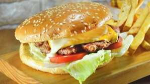 Een hamburger met sla, tomaat en kaas, en een portie friet op een houten plank.