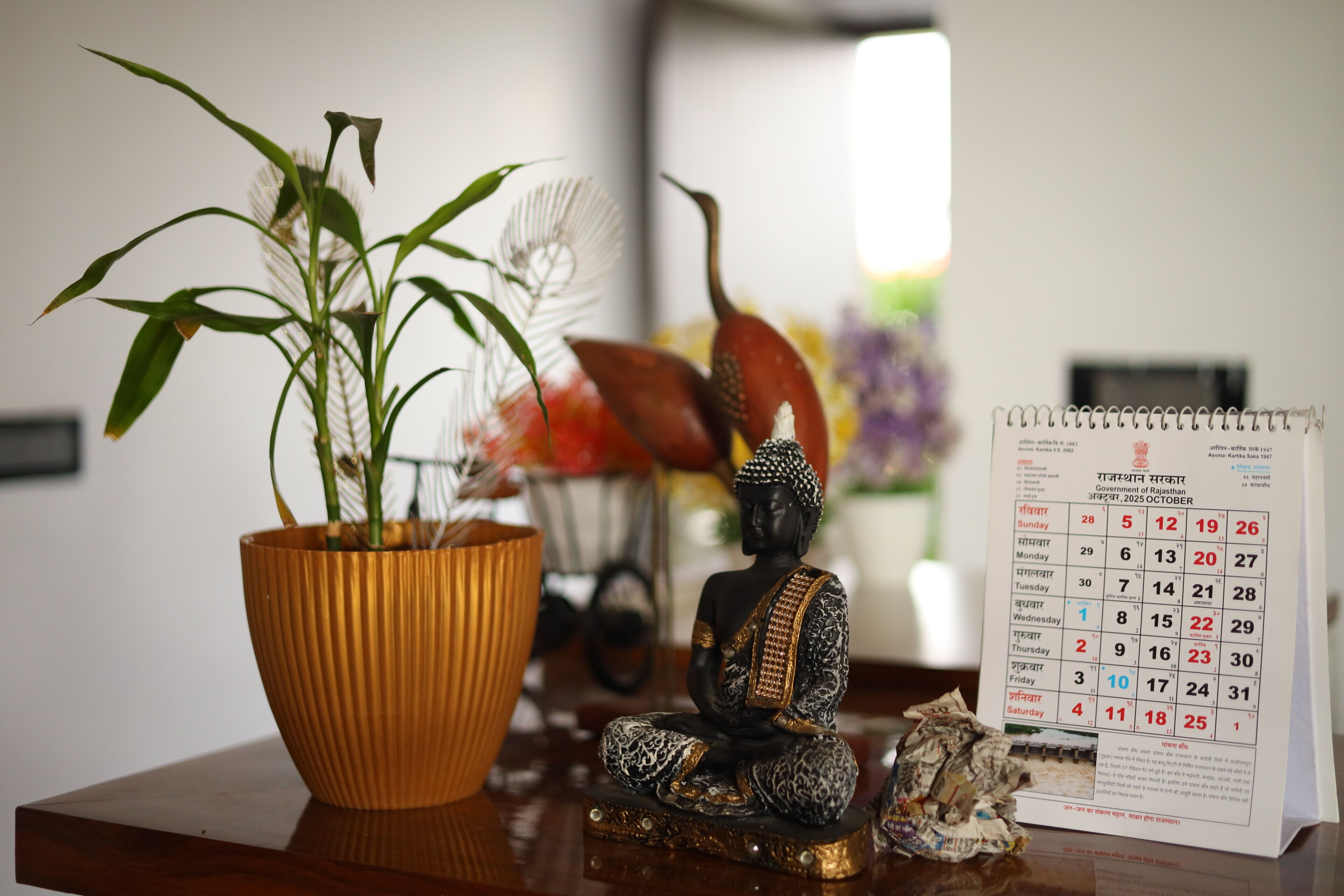 Una estatua de Buda, un calendario y una planta en maceta sobre una superficie de madera.
