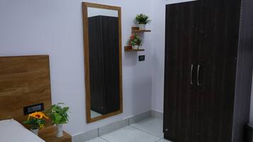 Un dormitorio con cama, un espejo grande, un armario y dos estantes pequeños con plantas.