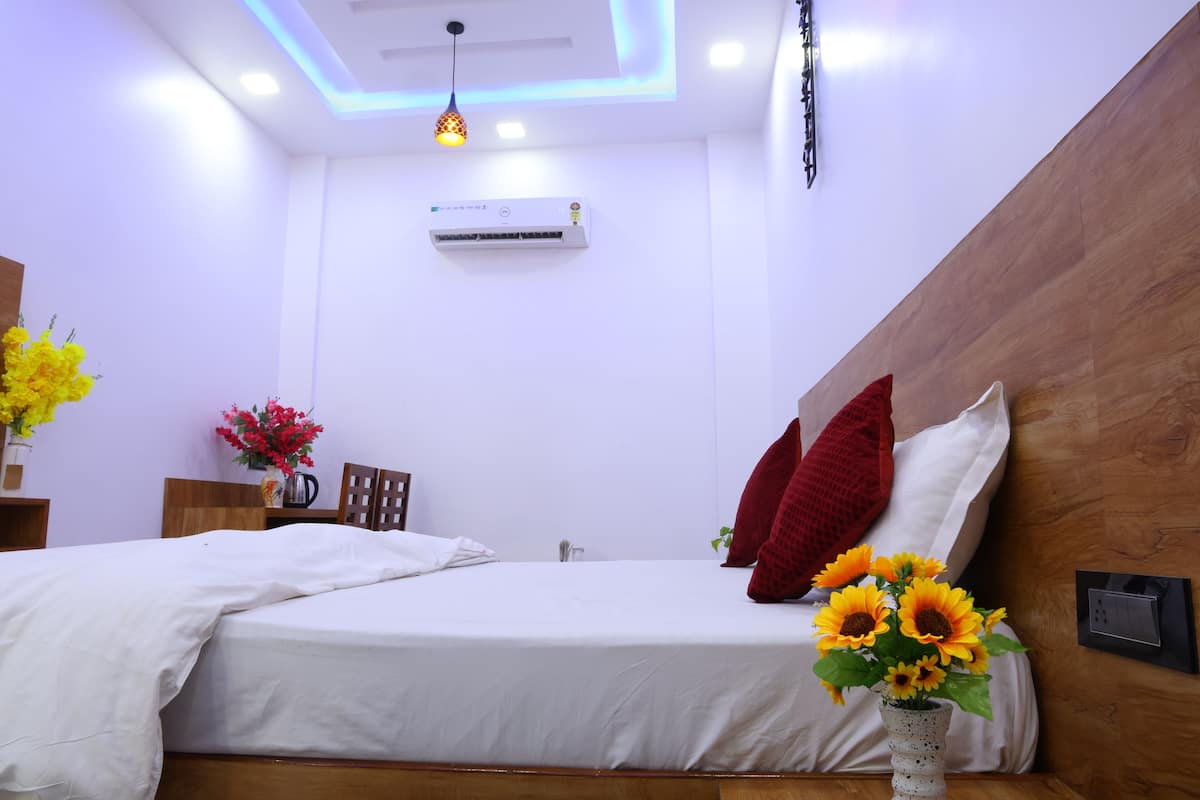 A modern bedroom with a wooden headboard, white bedding, a vase with sunflowers, and an air conditioning unit.