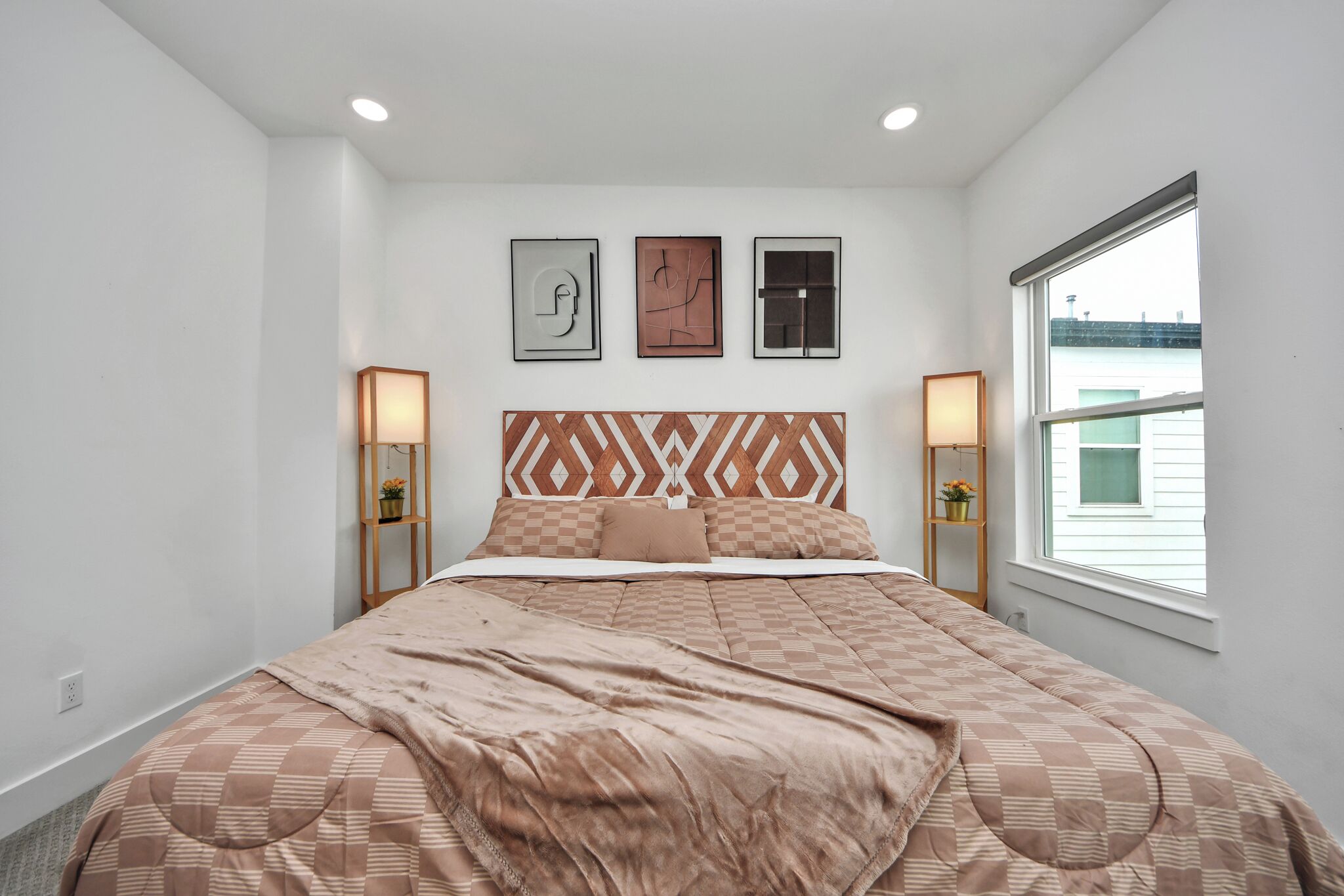 Une chambre à coucher avec un grand lit, deux tables de chevet avec des lampes, une tête de lit à motifs géométriques et trois œuvres d’art encadrées accrochées au mur.