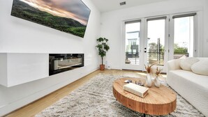 Uma sala de estar moderna com televisão de tela plana, lareira e uma janela grande com vista.