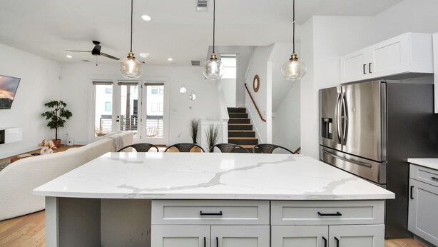 Uma cozinha moderna com uma ilha grande, eletrodomésticos de aço inoxidável e iluminação pendente.
