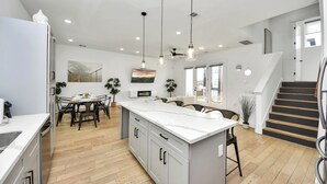 Uma cozinha moderna com ilha central, soalho de madeira e iluminação pendente.