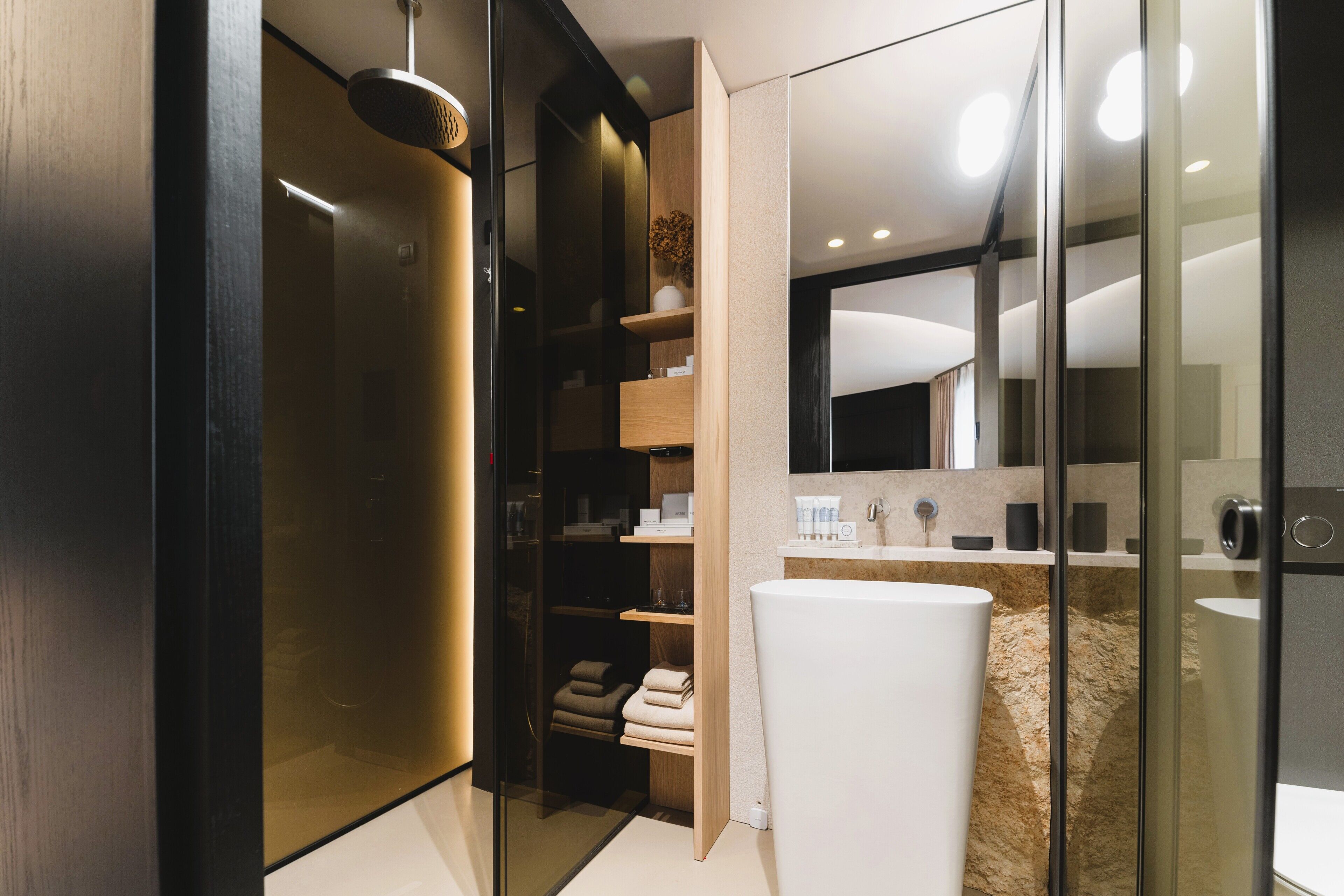 A modern bathroom with a glass shower enclosure, a built-in vanity, and a walk-in closet with shelves.