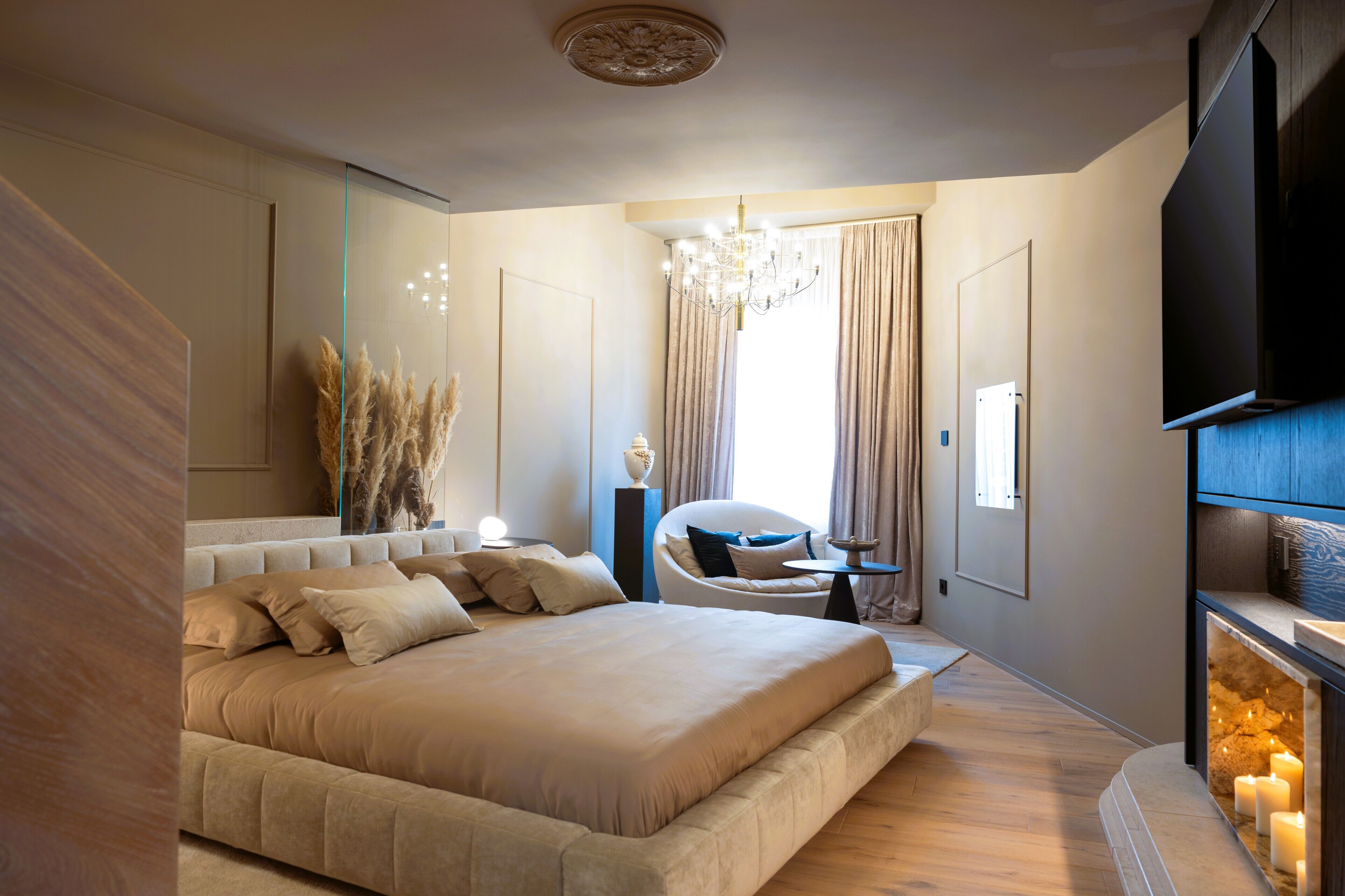 Une chambre moderne avec un grand lit, un lustre, une télévision et une cheminée.