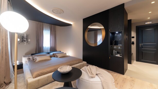 Et moderne hotelværelse med en stor seng, et rundt spejl, et lille bord og en mørk garderobe.