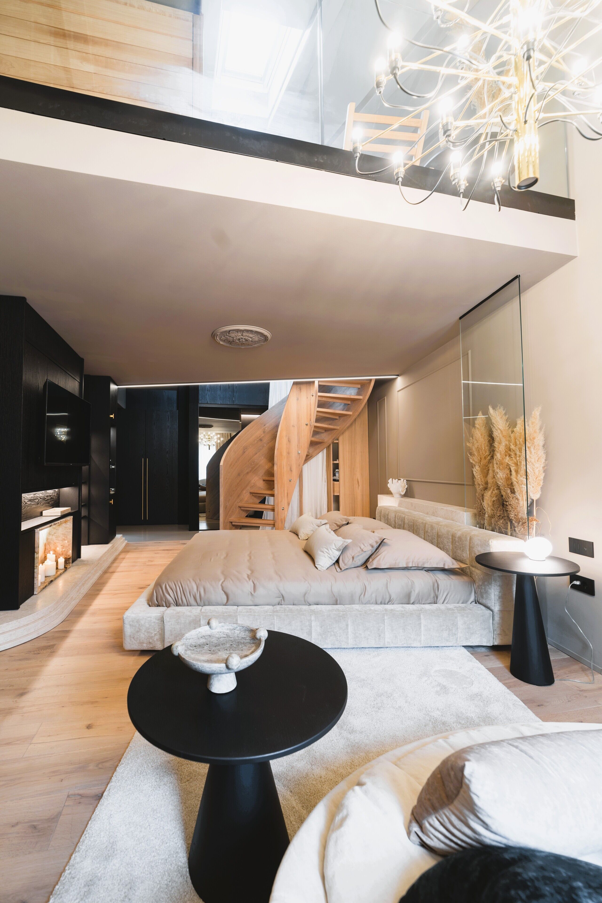 A modern interior with a bed, a round table, a staircase, and a large mirror.