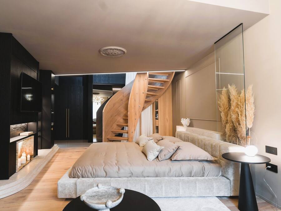 A modern interior with a bed, a round table, a staircase, and a large mirror.