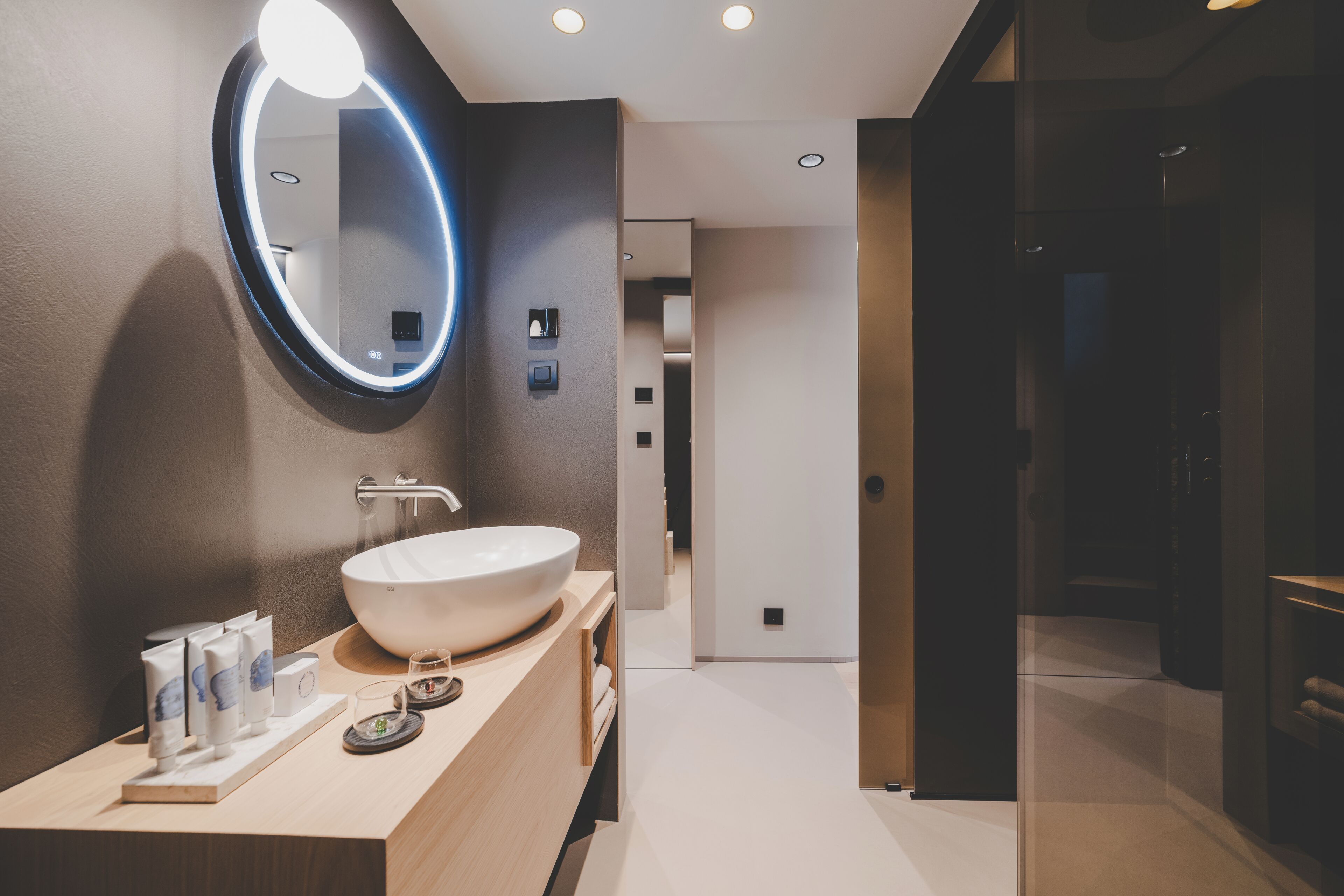 A modern bathroom with a large oval mirror, a white sink, and a wooden vanity.