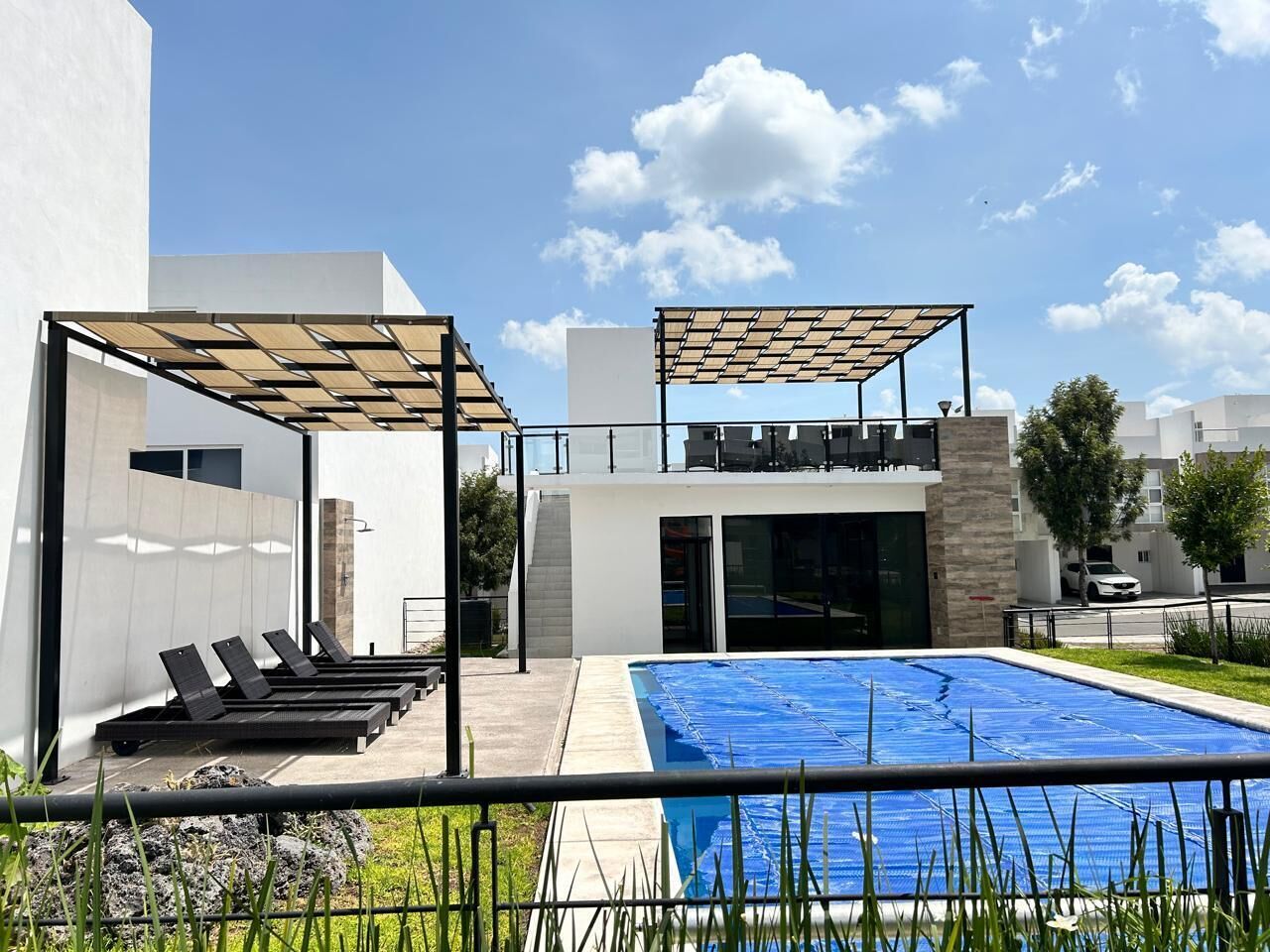 Un espace piscine extérieur moderne, doté de chaises longues et d’un coin salon abrité.