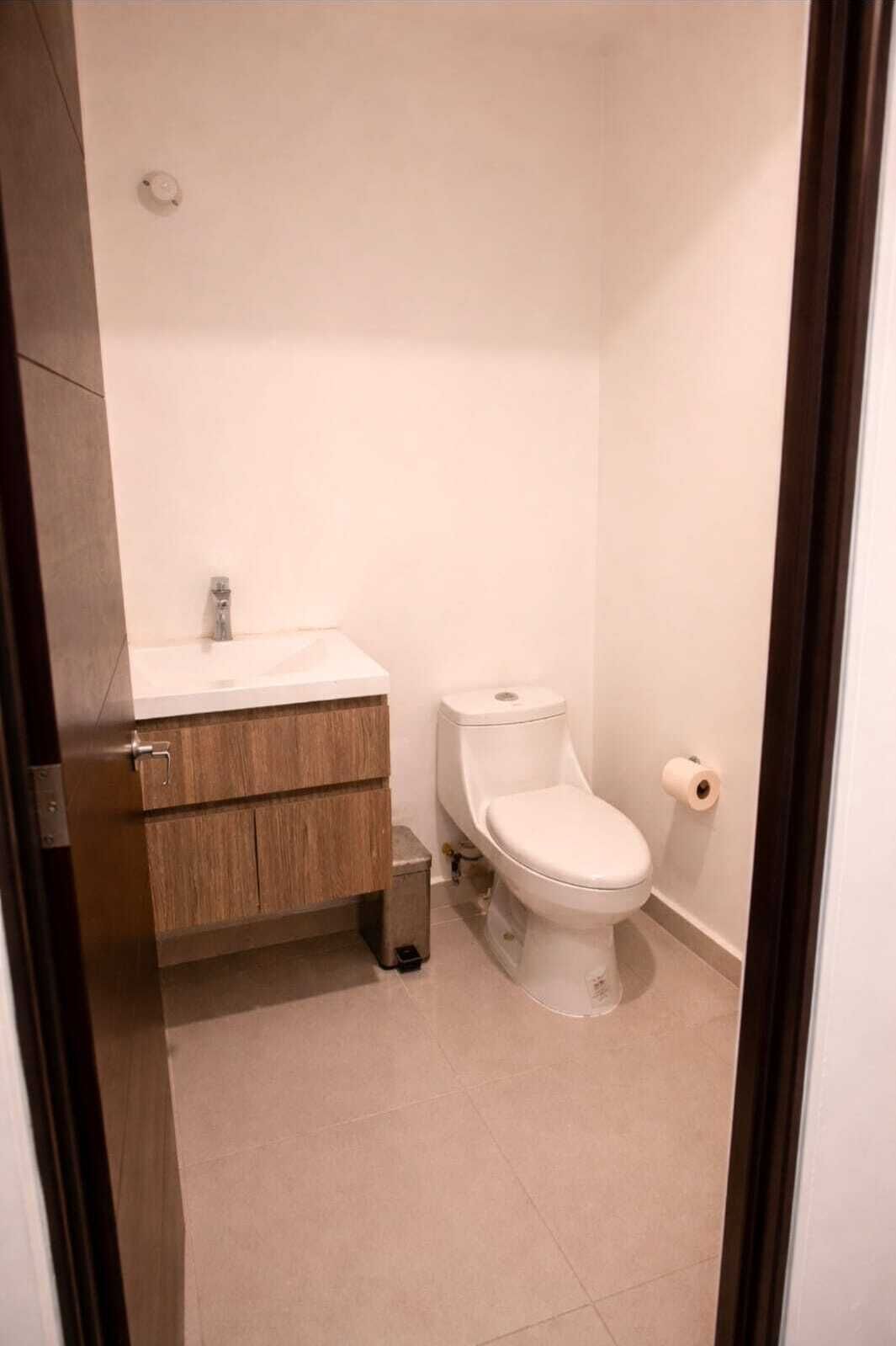 A small, clean bathroom with a toilet, a sink, and a roll of toilet paper.
