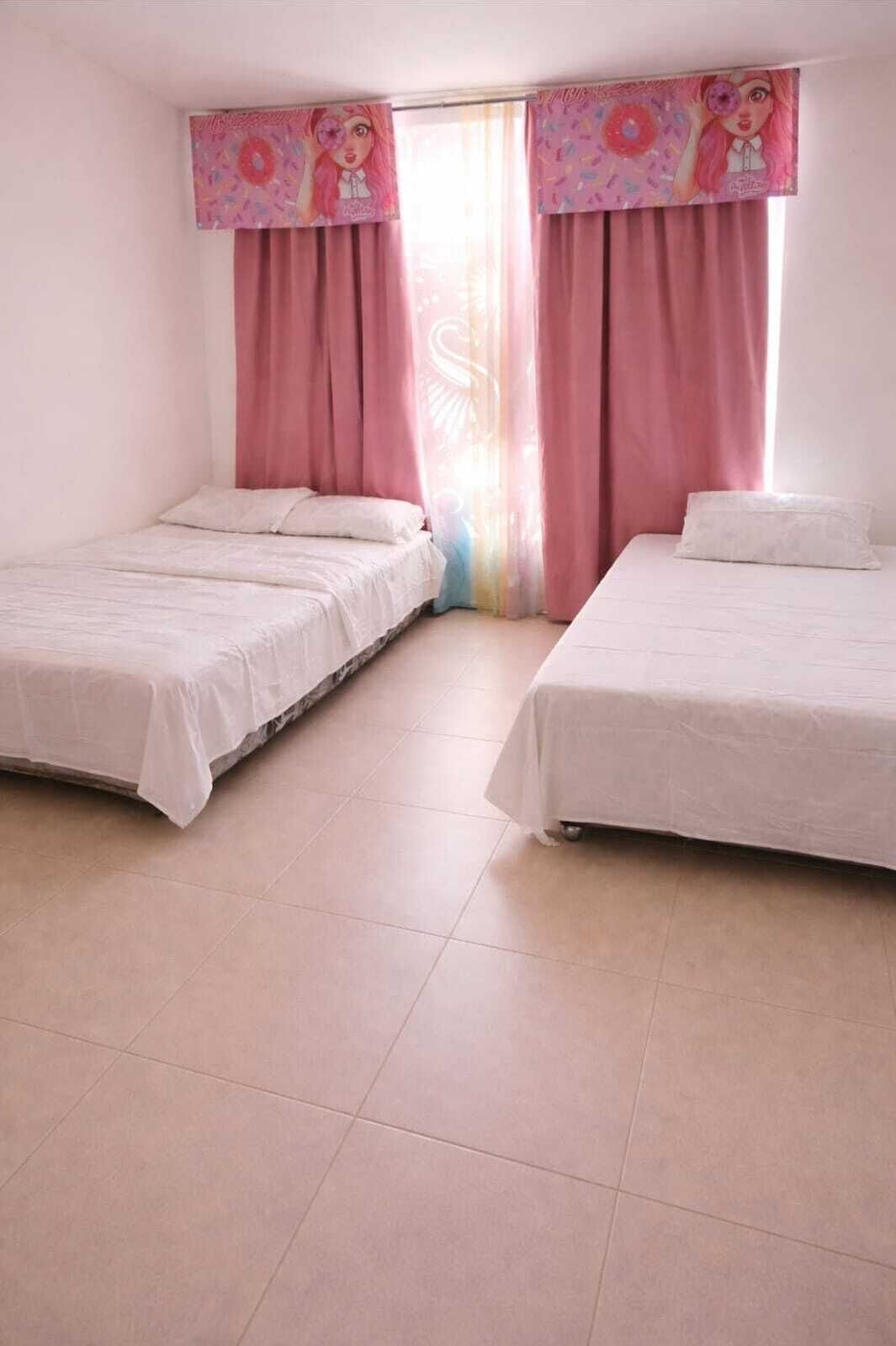 A room with two beds, pink curtains, and a window with a cartoon character.