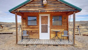 Una baita di legno con una porta d'ingresso, due finestre, un portico e due sedie.