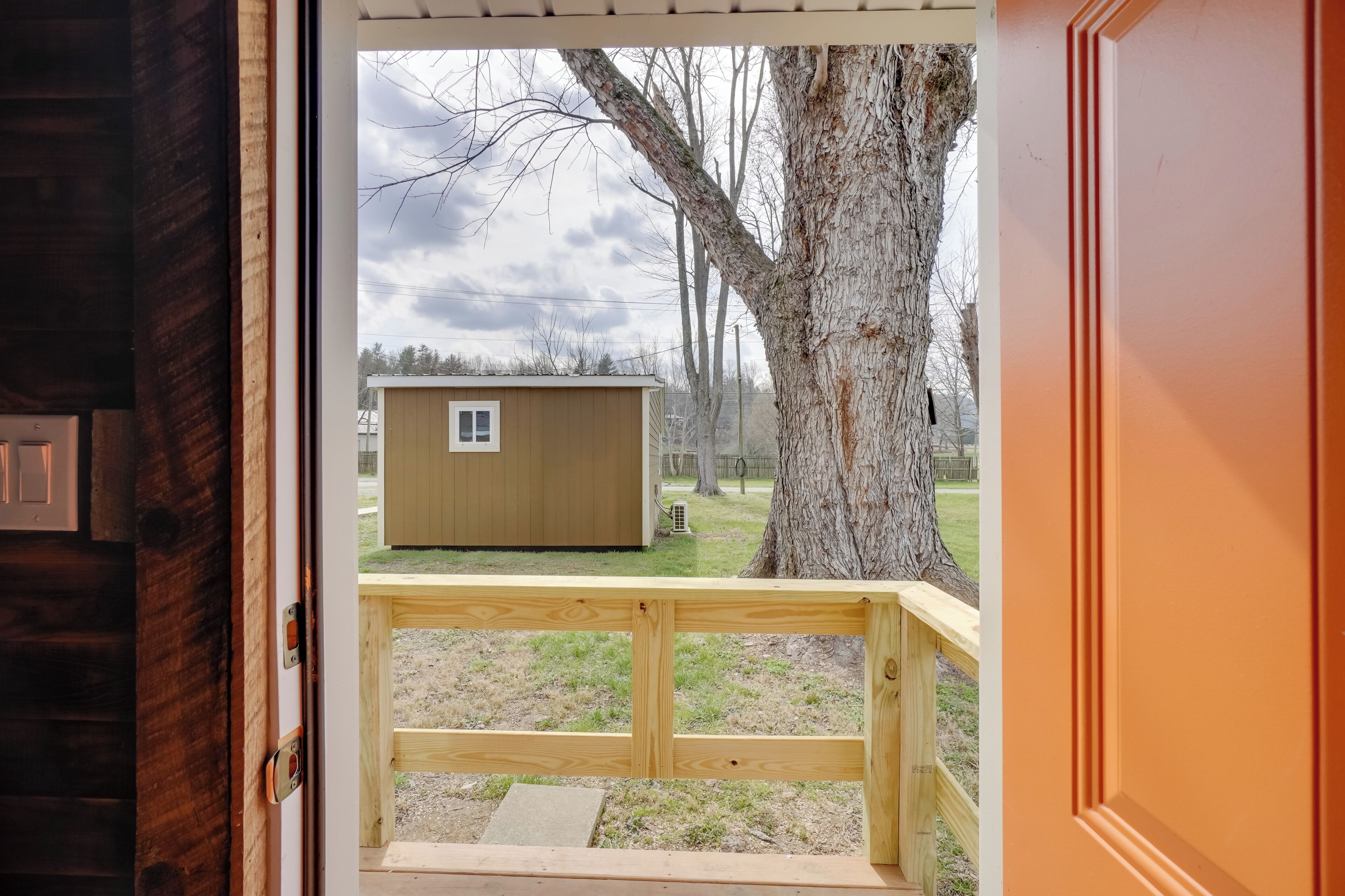 Une terrasse en bois offrant une vue sur un petit abri de jardin et un grand arbre.